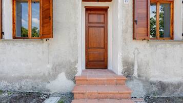 A building with a wooden door, two windows with wooden shutters, and a small set of steps leading to the entrance.