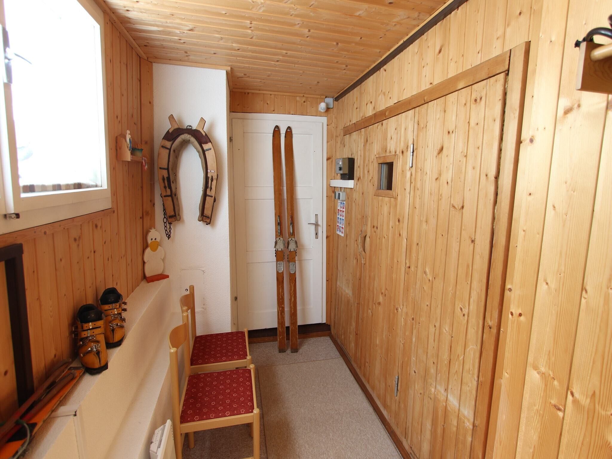 Et trægulvsrum med ski lænet op ad væggen, en stol og en dør.