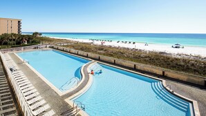 Une piscine située à côté d’une plage, avec des chaises longues et une vue sur l’océan.