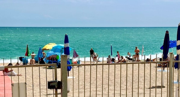 A beach with a fence, umbrellas, and people.