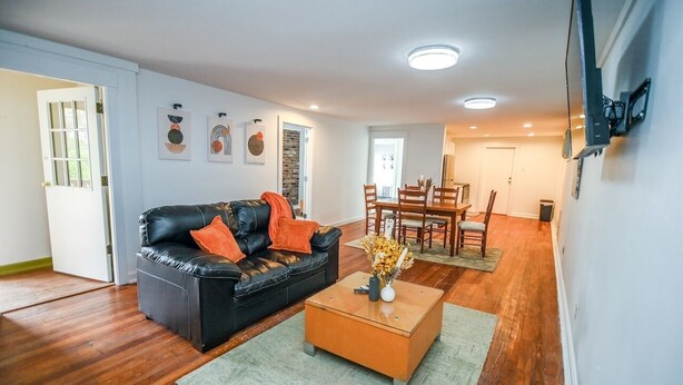 Ett vardagsrum med en svart lädersoffa, ett soffbord i trä och en matplats med trästolar och ett bord.