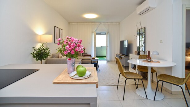 A modern living room with a dining area, a TV, and a view to the outside.