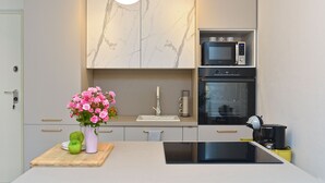 A modern kitchen with a marble backsplash, a built-in microwave, an oven, and a central island with a sink and a vase of flowers.