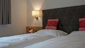 Une chambre d’hôtel avec deux lits, une table de chevet avec une bougie, une lampe fixée au mur et un coussin à carreaux.