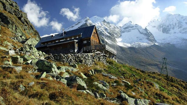 Un chalet de montagne avec des fondations en pierre, un revêtement extérieur en bois et une vue sur des sommets enneigés.