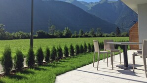 Une terrasse avec des sièges extérieurs donnant sur un champ verdoyant et des montagnes.
