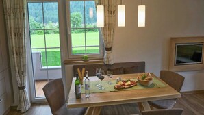 A dining area with a wooden table set for two, featuring a bottle of wine, glasses, and a bowl of bread and cheese.