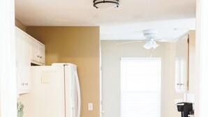 A kitchen with a refrigerator, oven, and dishwasher. There is a window with blinds and a ceiling fan.