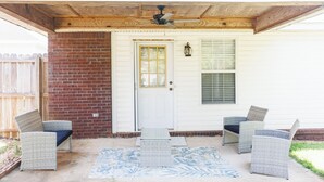 A covered porch with wicker furniture, a door, and a ceiling fan.