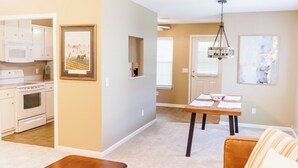 A modern kitchen with white appliances, a dining area with a wooden table, and a living room with a brown sofa.