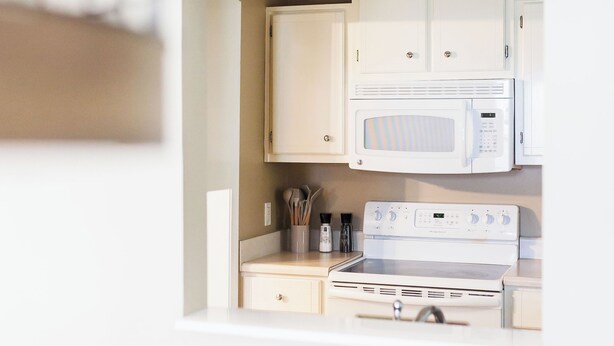 A compact kitchen with white appliances, including a microwave and a stove, and a small cabinet area.