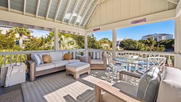 A covered outdoor seating area with a pool, cushioned seating, and a view of the surrounding greenery and buildings. - Spacious Second-Row Home Across from Beach Access (Georgetown)