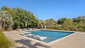 A rectangular swimming pool with a clear blue water surface, surrounded by a concrete deck. There are several lounge chairs and a small umbrella on the deck. - Spacious Second-Row Home Across from Beach Access (Georgetown)