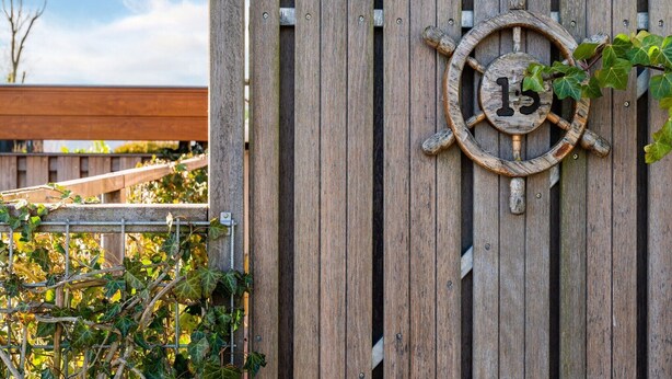 A wooden fence with a ship's wheel decoration and a metal gate. - Luxury Holiday Home in Bantega with Harbour and Sloop (Bantega)
