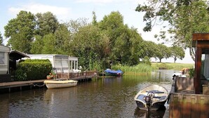 A calm canal with boats docked at wooden piers, surrounded by lush greenery and a small house. - Luxury Holiday Home in Bantega with Harbour and Sloop (Bantega)
