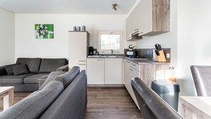 A compact living space with a grey sofa, a small kitchen area with a kettle, and a window providing natural light. - Luxury Holiday Home in Bantega with Harbour and Sloop (Bantega)