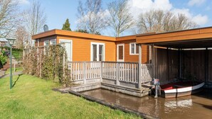 A wooden house with a fenced deck and a boat docked in a small water body. - Luxury Holiday Home in Bantega with Harbour and Sloop (Bantega)