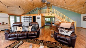 Ein geräumiges Wohnzimmer mit Ledersofas, einer Holzbalkendecke und einer Treppe, die zu einer oberen Ebene führt.