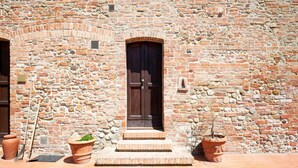 A stone building with a wooden door and steps leading to the entrance. There are terracotta pots on the ground. - Apartment in Peccioli with Pool and Wine Tasting (Peccioli)