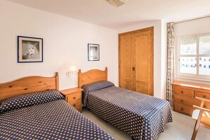 Ein Schlafzimmer mit zwei Einzelbetten, einem Holzschrank, einem Schreibtisch mit Stuhl und zwei gerahmten Bildern an der Wand.