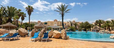 A pool area with lounge chairs, palm trees, and a clear blue sky.