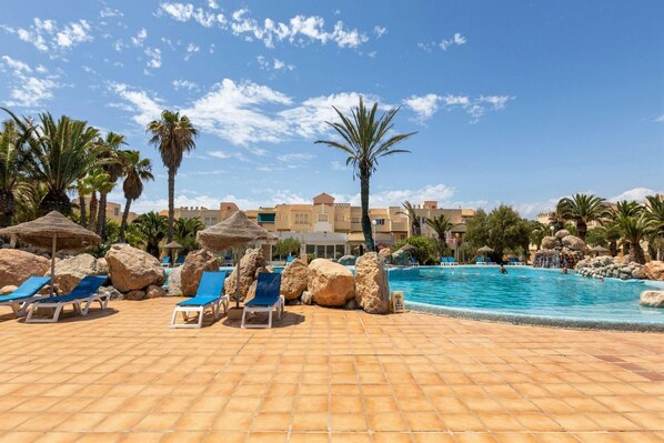 A pool area with lounge chairs, palm trees, and a clear blue sky.