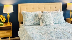 Ein Schlafzimmer mit einem gebogenen Kopfteil, einer gemusterten Bettdecke und zwei floralen Bildern an der Wand.