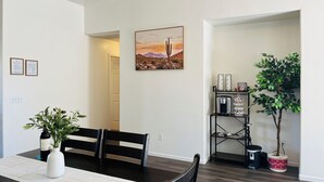 Ein Essbereich mit Tisch, Stühlen, einer Pflanze in einer Vase, einem Bild an der Wand und einer Kaffeestation.