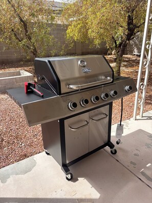 Una parrilla de gas portátil con cuatro quemadores, repisa lateral y ruedas.