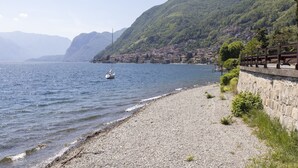 Ein Kiesstrand mit einer Steinmauer und einem Boot auf dem Wasser.