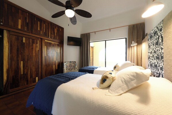A hotel room with a large bed, a ceiling fan, a flat-screen TV, and a window with curtains.