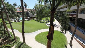 A resort courtyard with palm trees, a pool, and a thatched-roof structure.