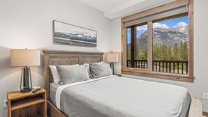 Un dormitorio con cama, dos mesitas de noche con lámparas, un cuadro en la pared y una ventana con vistas a la montaña.