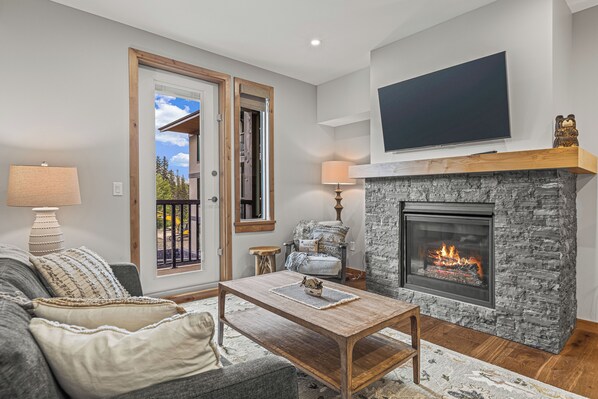 A living room with a fireplace, a sofa, a coffee table, and a TV mounted on the wall.