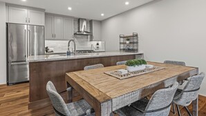 Una cocina moderna con electrodomésticos de acero inoxidable, una mesa de comedor de madera y sillas tapizadas en gris.