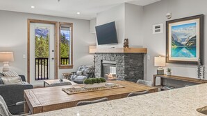 Una sala moderna con chimenea, un televisor de pantalla plana montado encima y un comedor con mesa y sillas de madera.