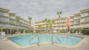 A swimming pool with a stone waterfall feature, surrounded by a multi-story hotel with balconies and palm trees. - Beach Hair; Don't Care - Waves, Views, and Zero Worries! (Galveston)
