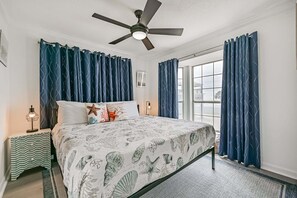 Un dormitorio con cama, cortinas, ventilador de techo, mesita de noche y ventana.