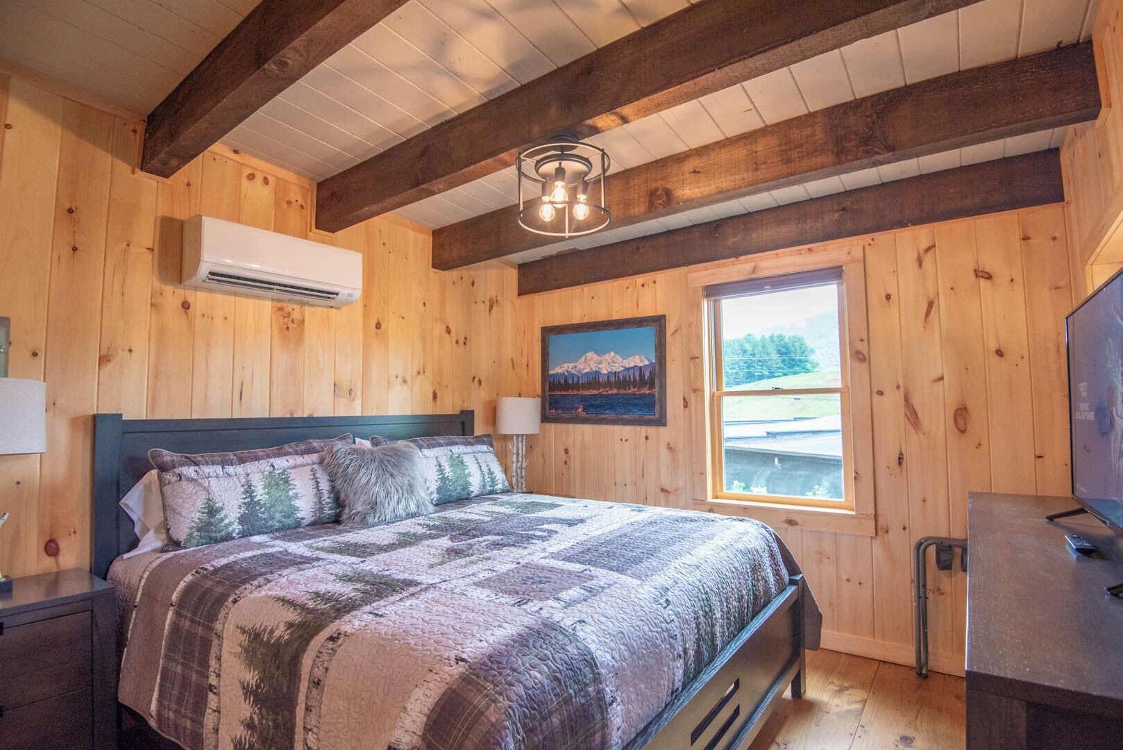 Ein Schlafzimmer mit Holzwänden, einem Bett, einem Wandfernseher und einem Fenster mit Blick auf die Landschaft.