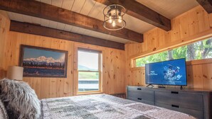 A cozy wooden room with a bed, a television, and a window with a view of greenery.