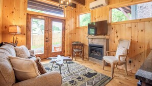 A cozy cabin interior with a sofa, fireplace, television, and a patterned rug.