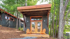 A cabin with a wooden deck, two Adirondack chairs, and a large glass door.