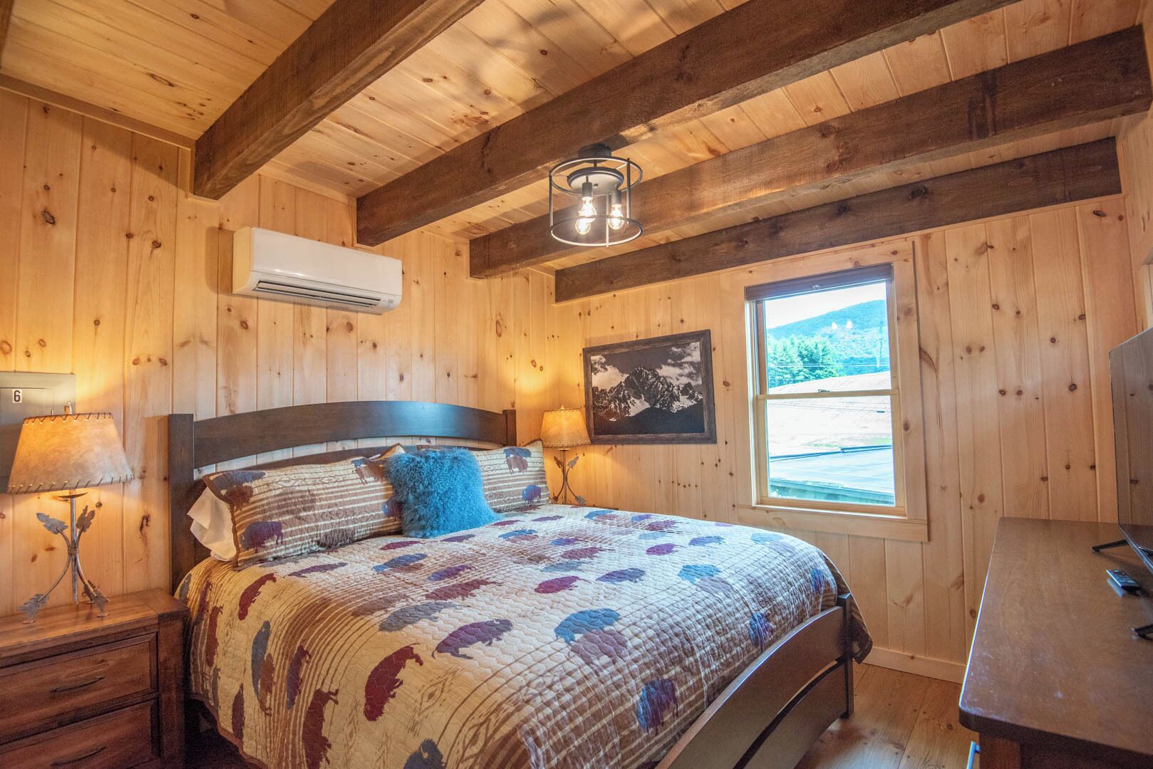 Ett sovrum i en stuga med träpanel, inrett med en säng, två sängbord, ett skrivbord och ett fönster med utsikt över bergen.