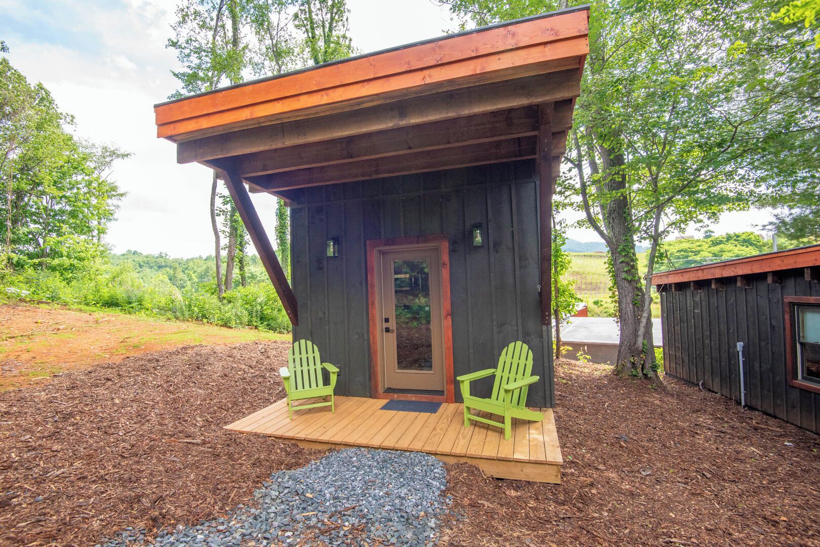 Eine kleine Holzhütte mit Veranda, zwei Adirondack-Stühlen und einem Kiesweg.