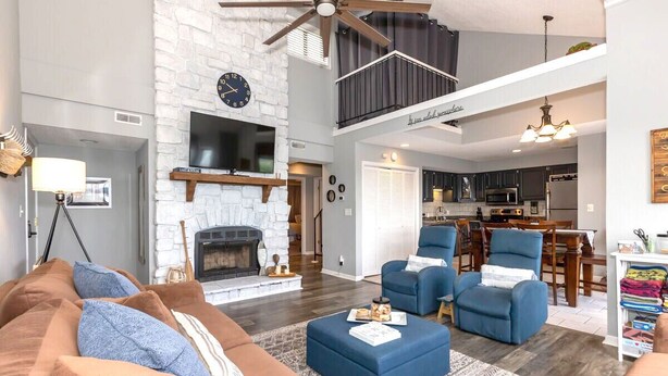 A spacious living room with a fireplace, blue armchairs, a sofa, and a dining area with a kitchen in the background.