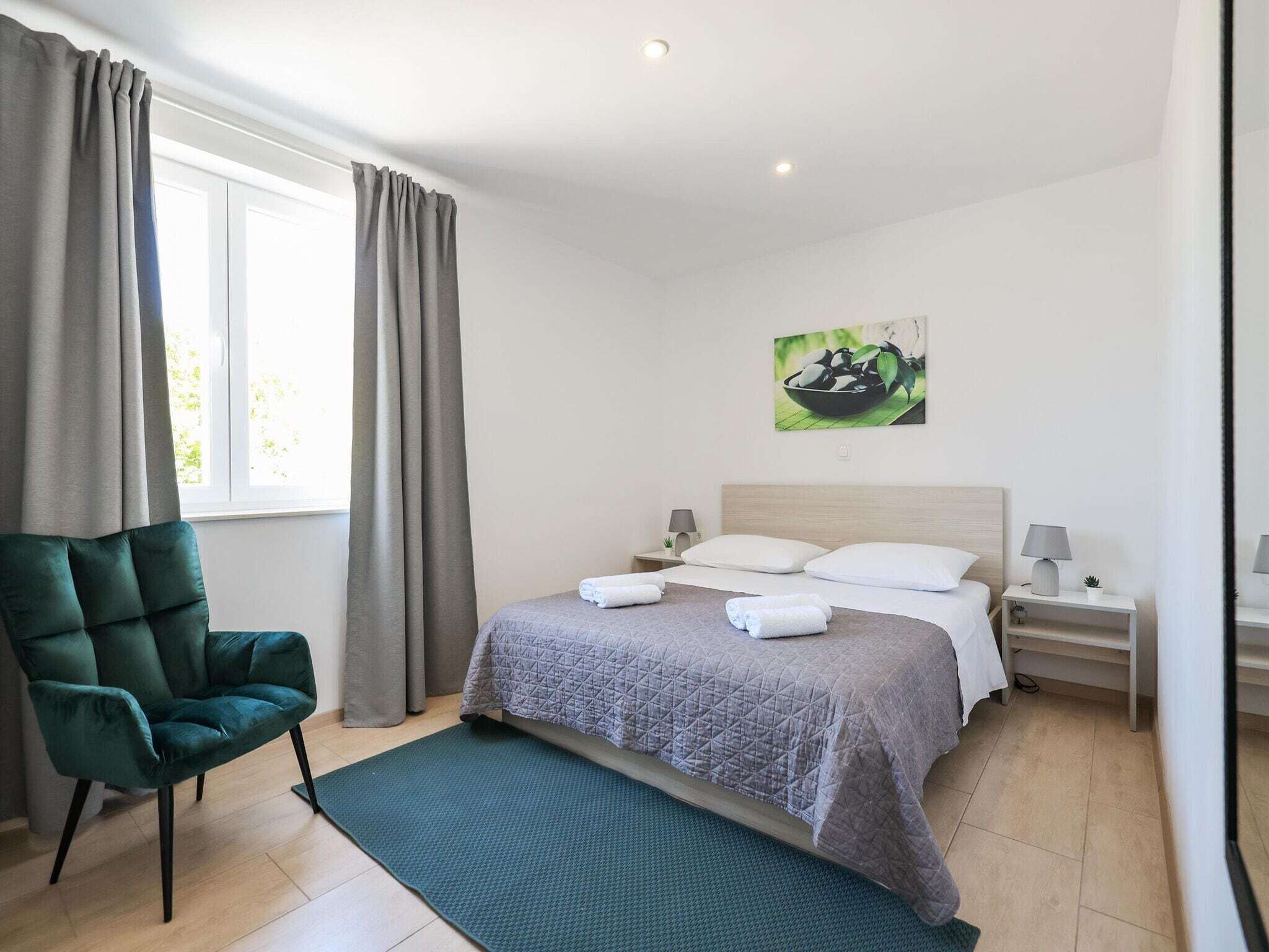 Une chambre à coucher moderne avec un lit, un fauteuil vert, une table de chevet avec une lampe et un tableau au mur.