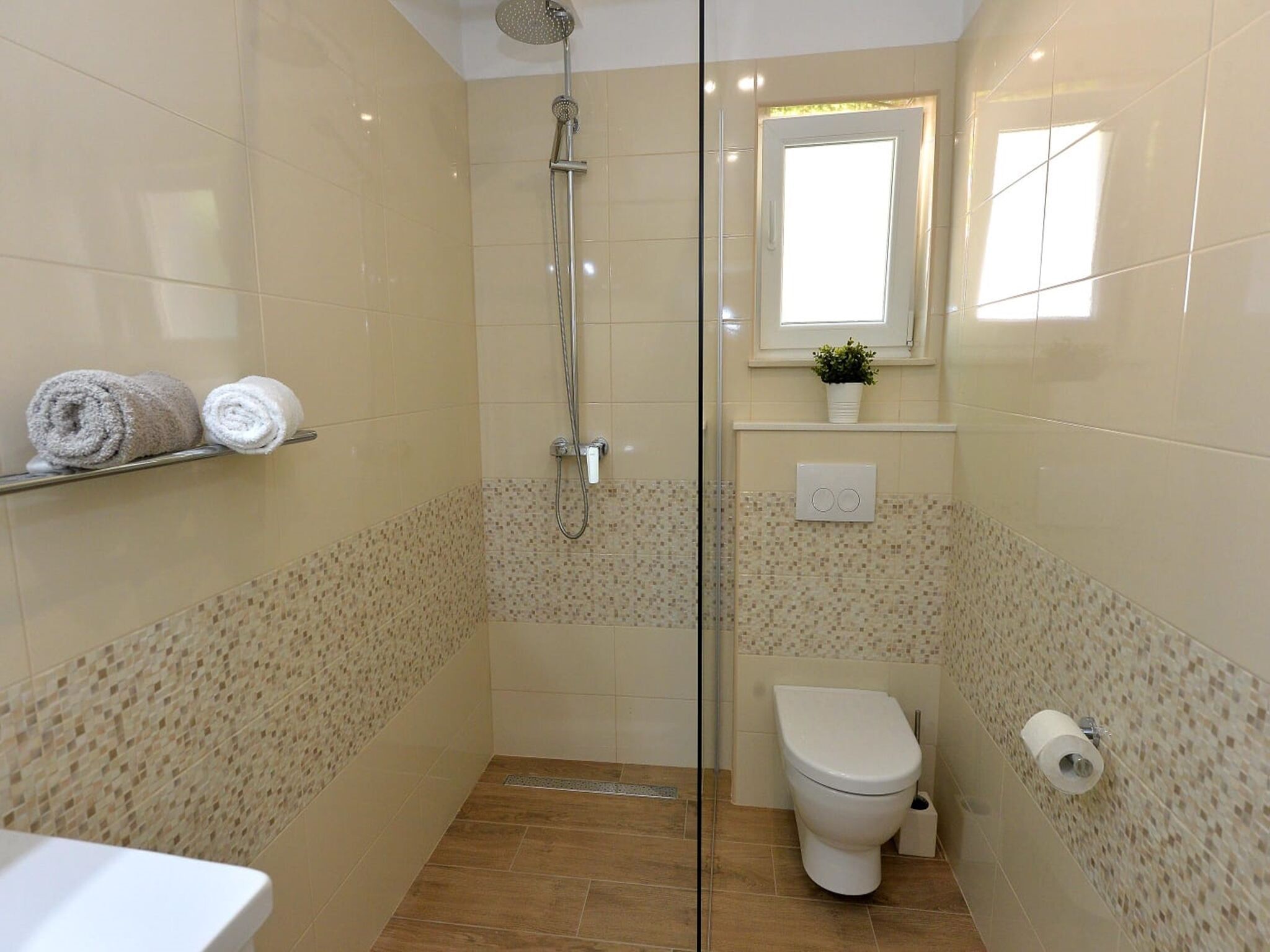 A bathroom with a shower, toilet, and a shelf with towels.