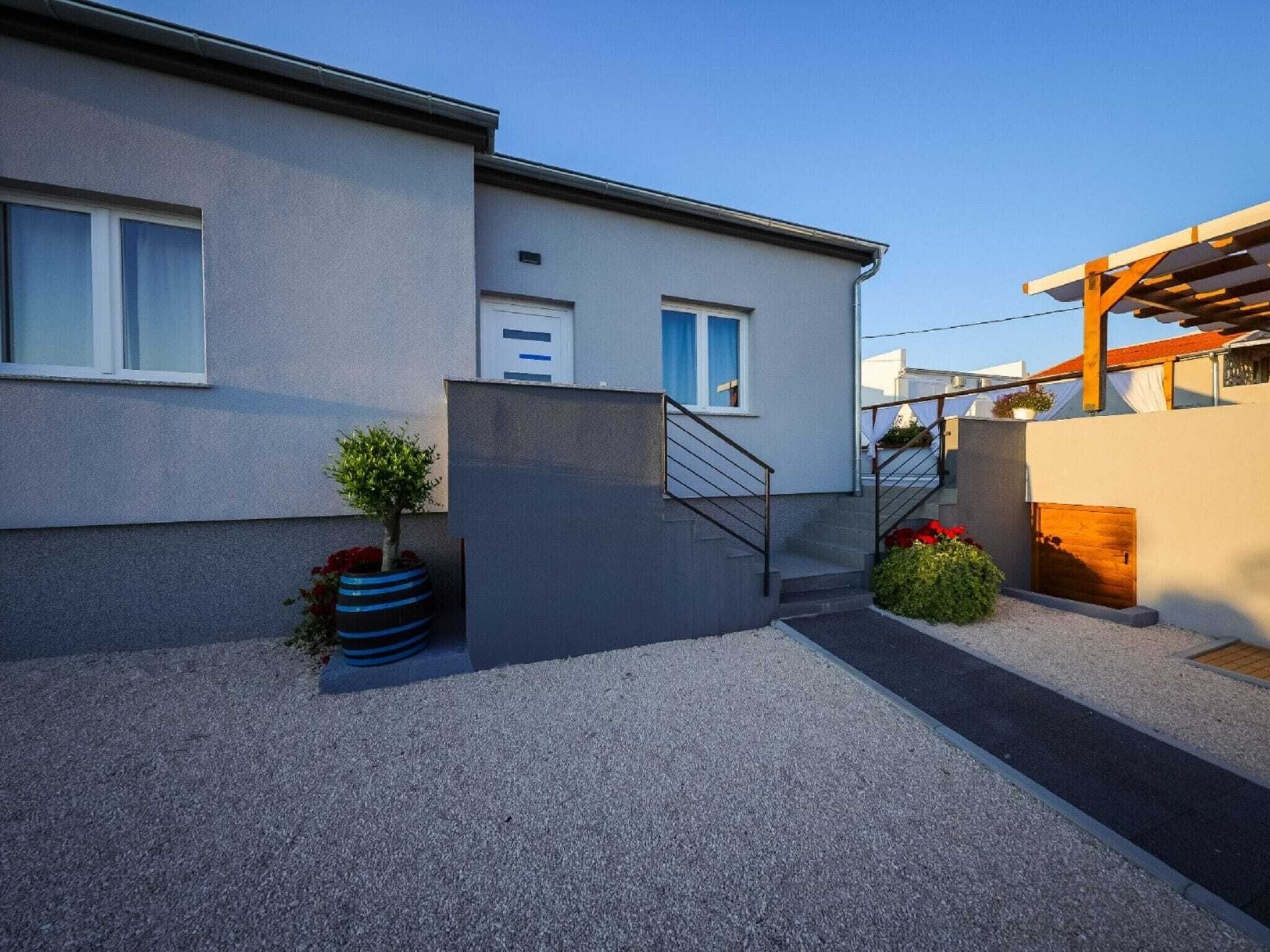 A modern building with a grey exterior, a small staircase, and a wooden pergola.