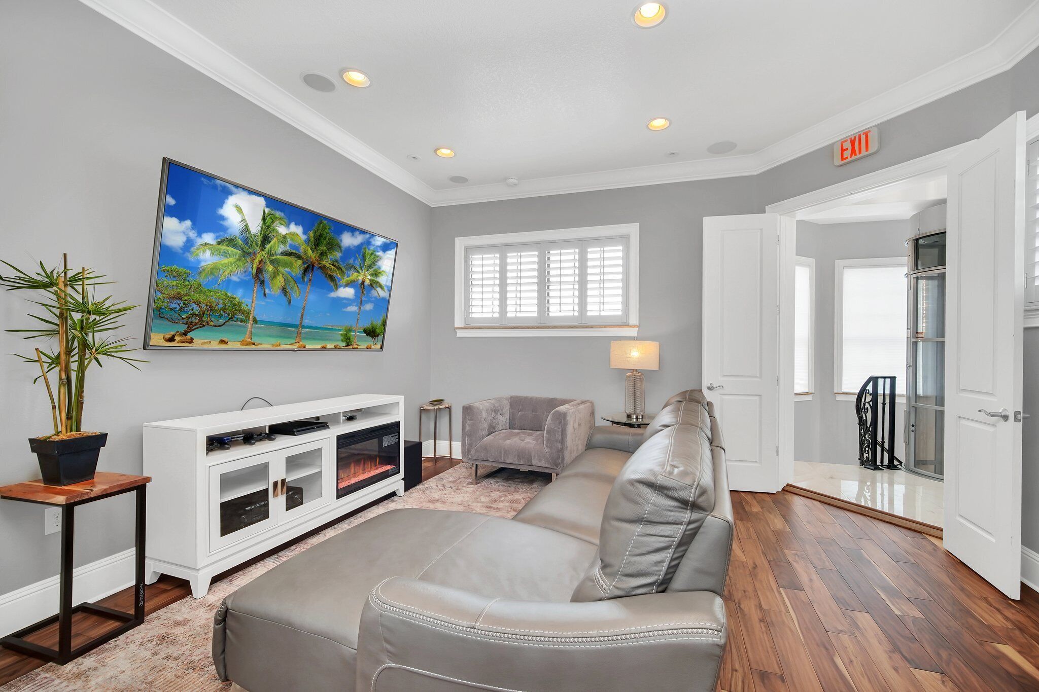 A modern living room with a fireplace, a large painting of a beach, a grey sofa, and a white entertainment unit.