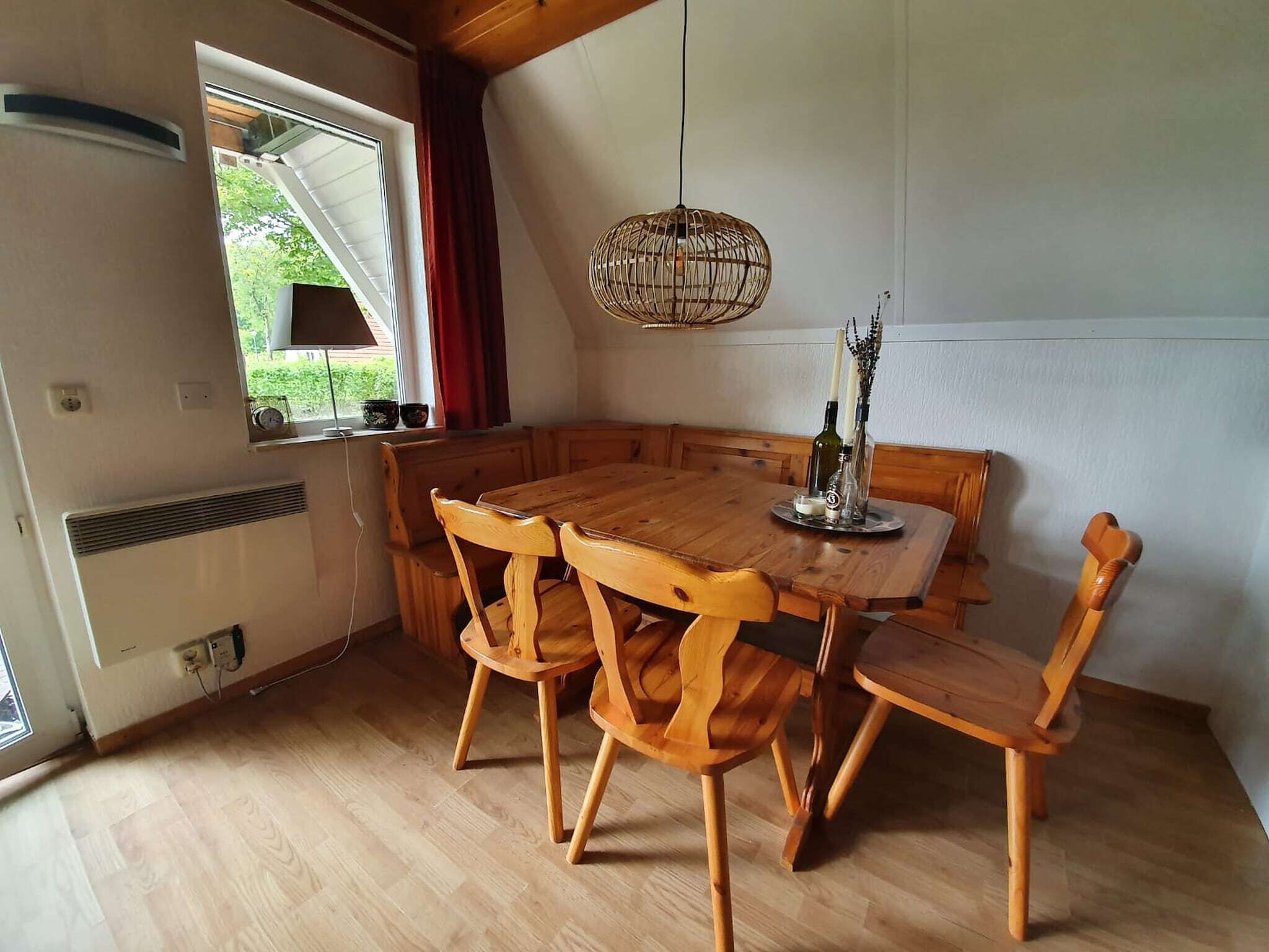 Ein Essbereich mit einem Holztisch und Stühlen, einer Hängelampe und einem Fenster mit Vorhängen.